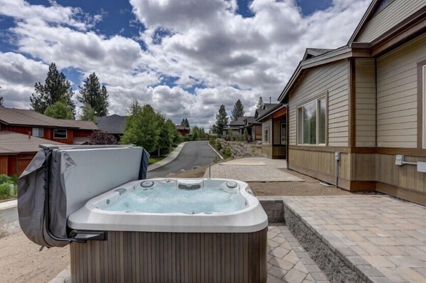 A hot tub in a residential setting with a paved driveway and wooden houses in the background.