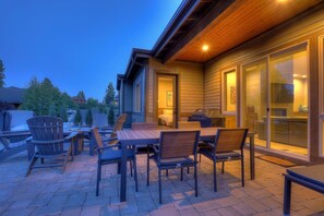 An outdoor patio with a wooden table and chairs, a covered seating area, and a sliding glass door leading to a kitchen. - Kangaroo Loop - Closest to Bachelor! 5BR/3.5BA, Jacuzzi (Bend)