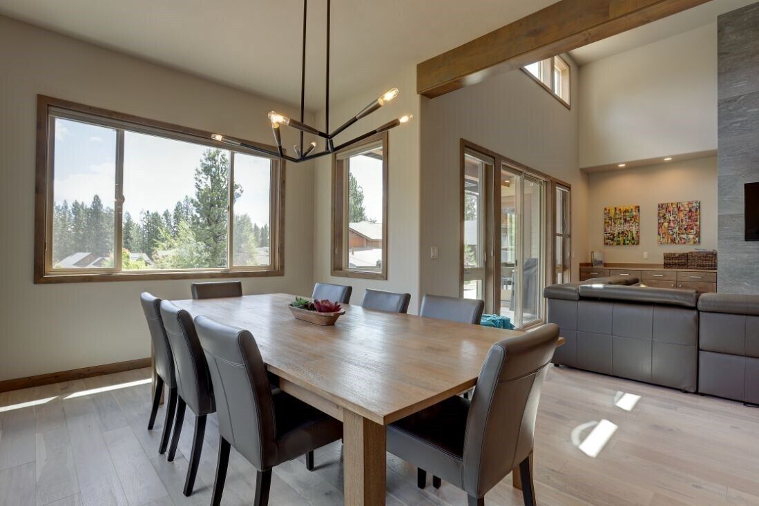 Una cocina moderna con comedor, ventanas amplias y vista a árboles.
