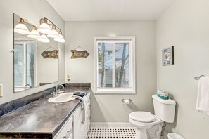 A bathroom with a sink, mirror, toilet, and window with blinds.