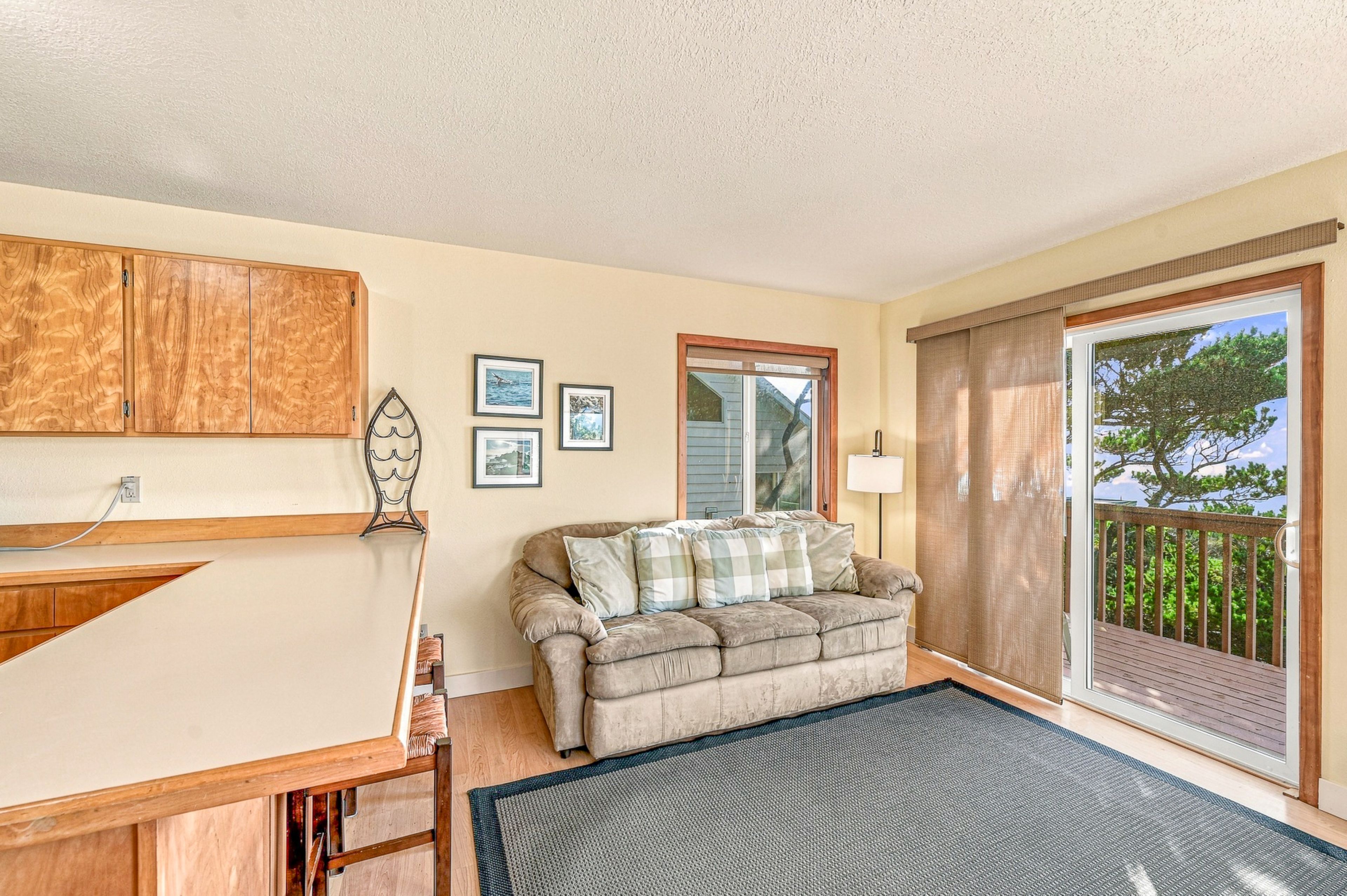A cozy living room with a wooden cabinet, a cushioned sofa, a small table, and a view through a sliding glass door.