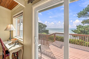 A room with a view of the ocean, a wooden deck, a table with a lamp, and a chair.