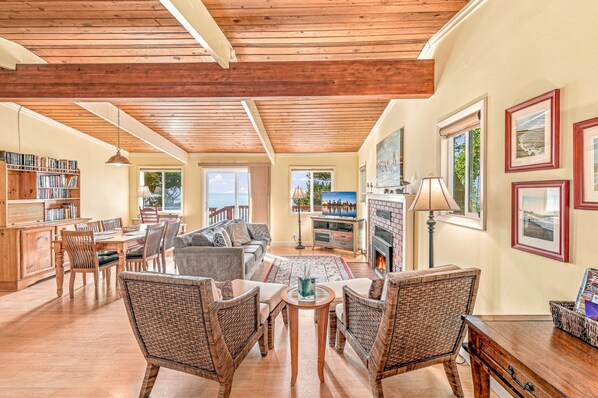 A spacious living room with a high ceiling, wooden beams, a fireplace, a television, and a bookshelf.