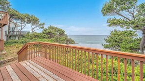 Une terrasse en bois dotée d’une rambarde, qui offre une vue sur une zone côtière bordée d’arbres et sur l’océan.