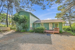 A two-story house with a green exterior, a front porch, and a gravel driveway.