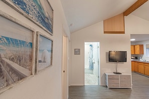 Stylish hallway leads to a bathroom with shower and toilet, featuring framed artworks and a mounted TV.