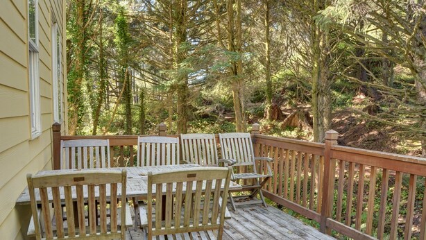 Une terrasse en bois avec une table et des chaises, entourée d’arbres.