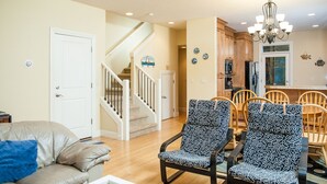Un salon avec un canapé beige, des fauteuils à motifs, un escalier et un coin cuisine.