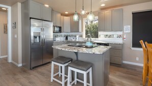 A modern kitchen with grey cabinets, a stainless steel refrigerator, a granite countertop, and two bar stools.