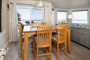 En matplats med ett bord och stolar, en soffa och stora fönster med utsikt över havet.