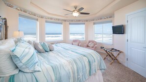 A bedroom with a large bed, a ceiling fan, and a view of the ocean through large windows.