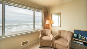Ein Zimmer mit zwei beigefarbenen Sesseln, einer Lampe, einem Spiegel und Meerblick.