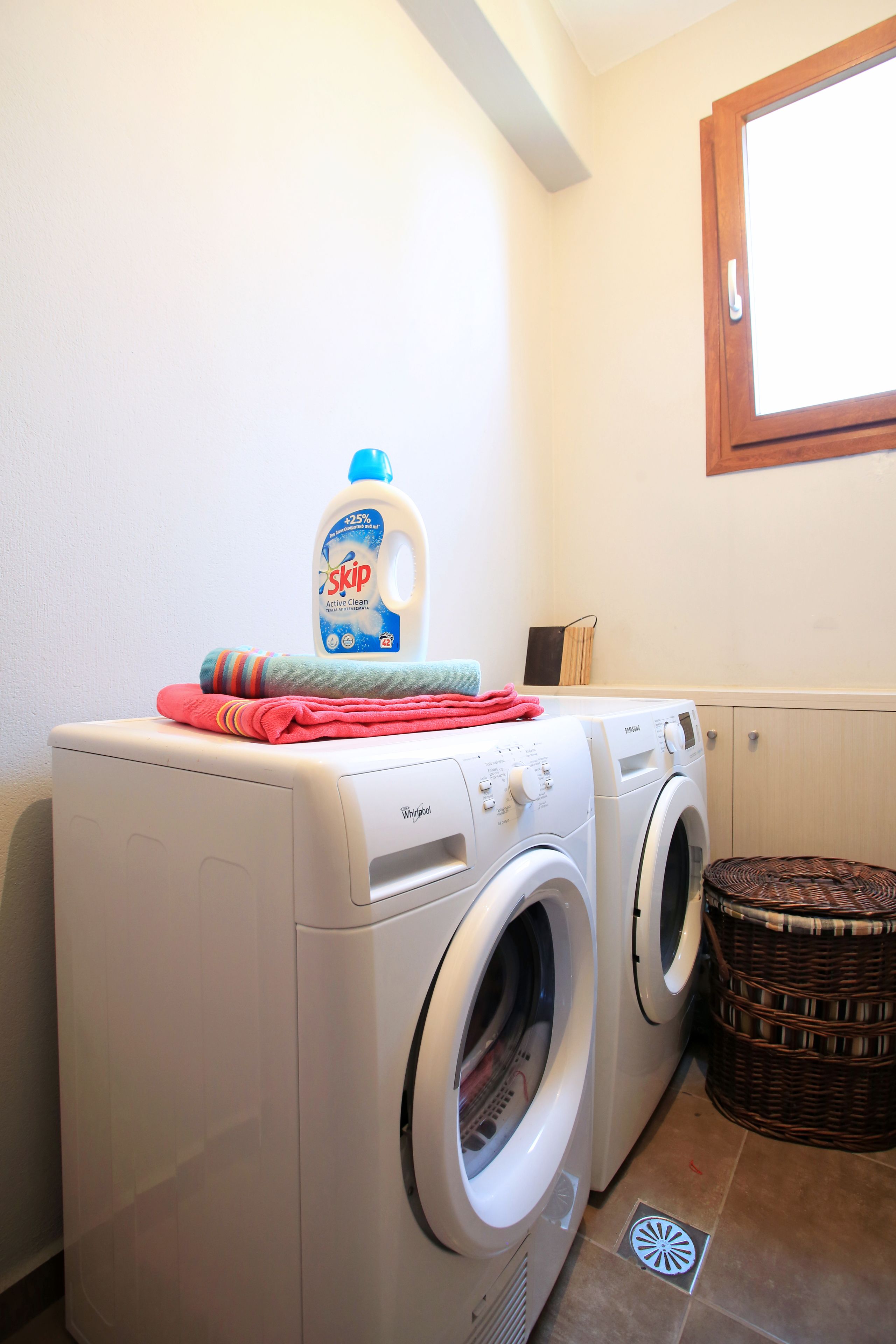 Un espace dédié à la lessive, comprenant deux machines à laver à chargement frontal, une bouteille de lessive, une serviette pliée et un panier en osier.