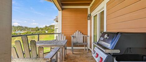 A covered patio with a grill, wooden chairs, and a table.