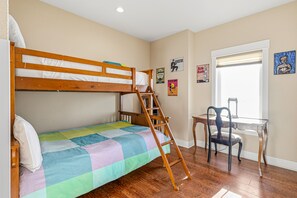 Een stapelbed met een ladder, een bureau met een stoel en diverse decoraties aan de muur in een kamer met houten vloer.