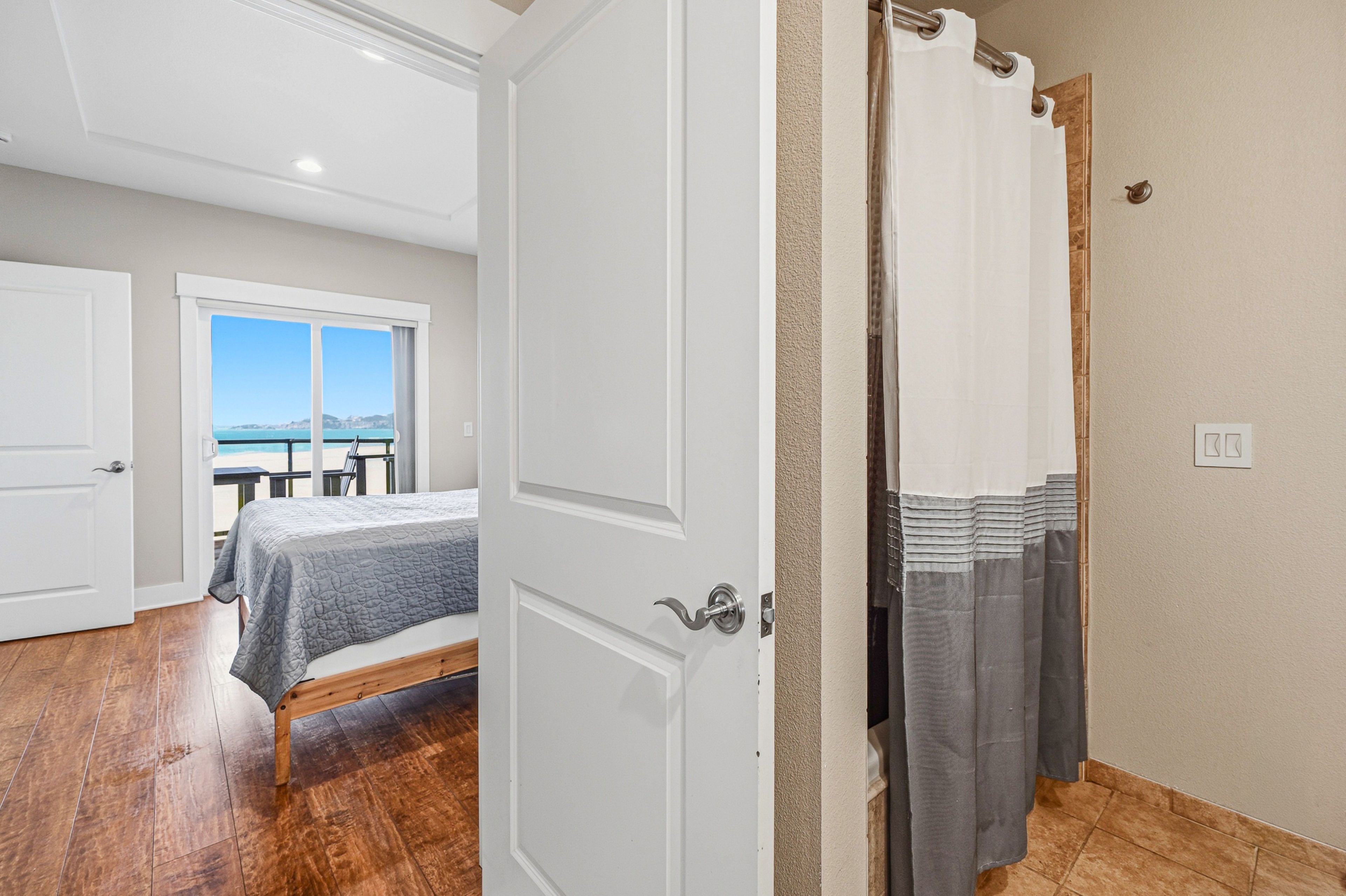 You'll find crisp white doors and warm wood floors framing your space, while the nearby bedroom invites you to rest with stunning ocean views just beyond the window.