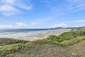 Een kustlandschap met een strand, begroeiing en een verre heuvel met gebouwen.