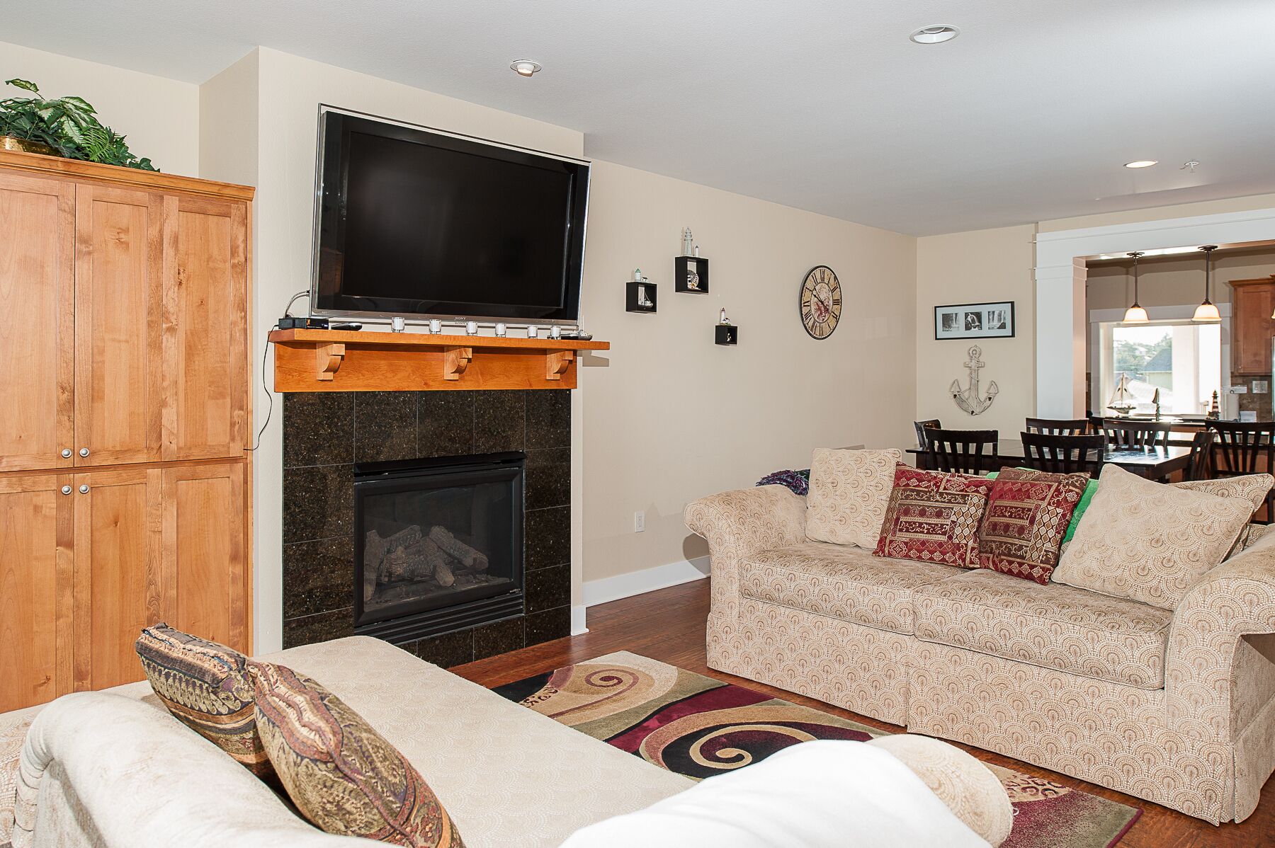 A living room with a fireplace, a television mounted above it, a dining area with a table and chairs, and a sofa with patterned cushions.