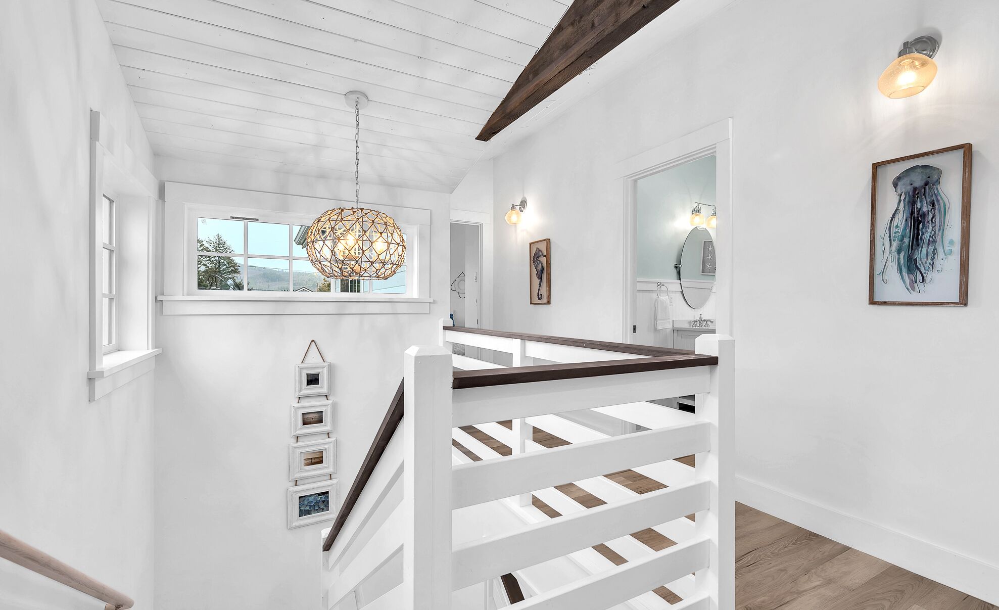 Een witte binnenruimte met een houten trap, een hanglamp en lijstwerken aan de wanden.