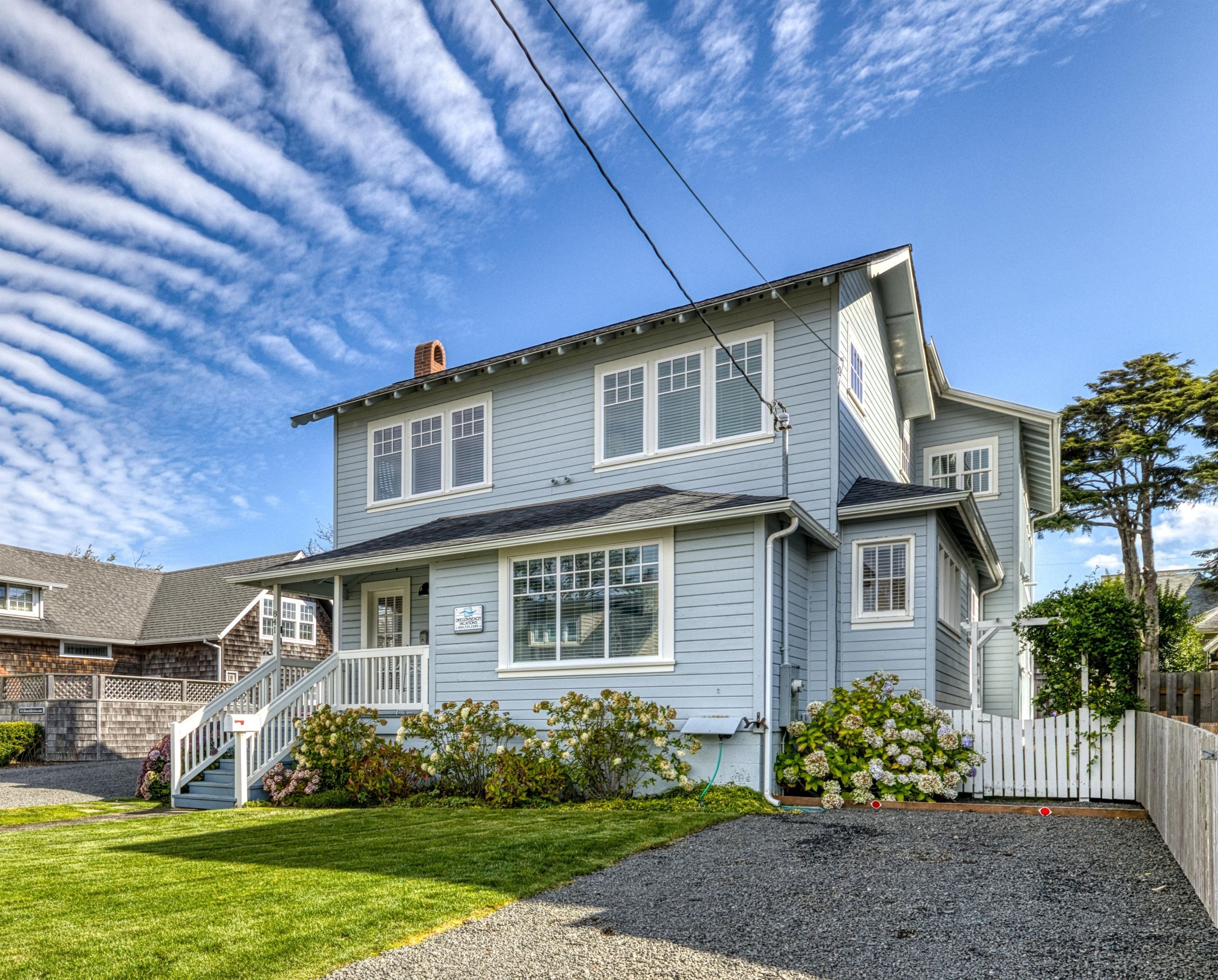 A charming coastal home awaits, featuring a covered front porch and manicured lawn beneath dramatic cloud-streaked skies—your welcoming retreat by the sea.
