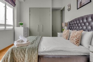 A neatly made bed with a tufted headboard, a bedside table with a lamp, and a wardrobe with sliding doors. - One bedroom apartment City Road (London)