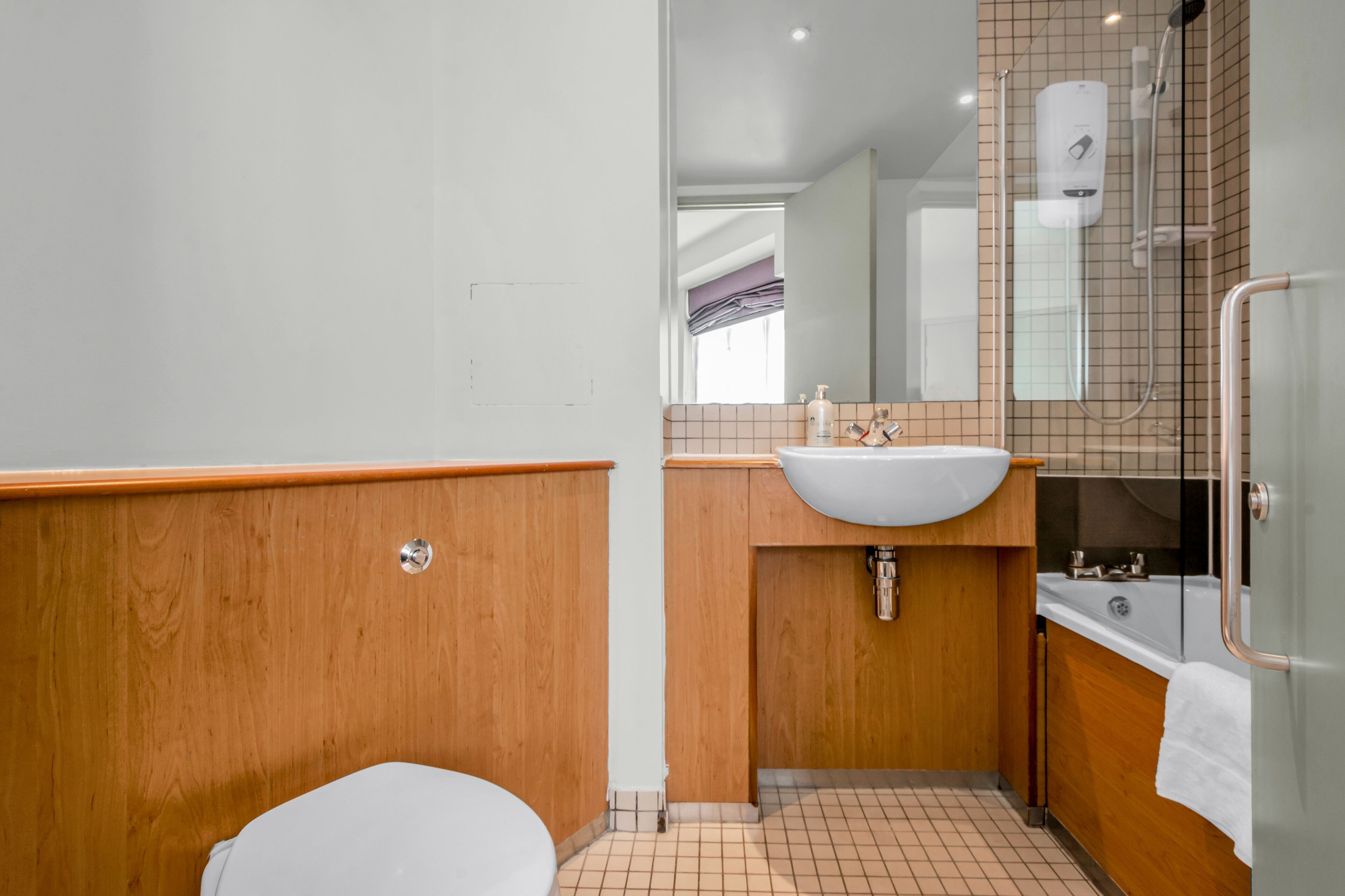 A bathroom with a wooden vanity, a white sink, a glass shower enclosure, and a white toilet.