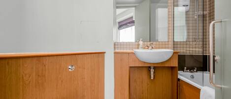 A bathroom with a wooden vanity, a white sink, a glass shower enclosure, and a white toilet.