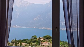 Une vue à travers une fenêtre avec des rideaux, donnant sur un lac, des montagnes et une ville côtière.