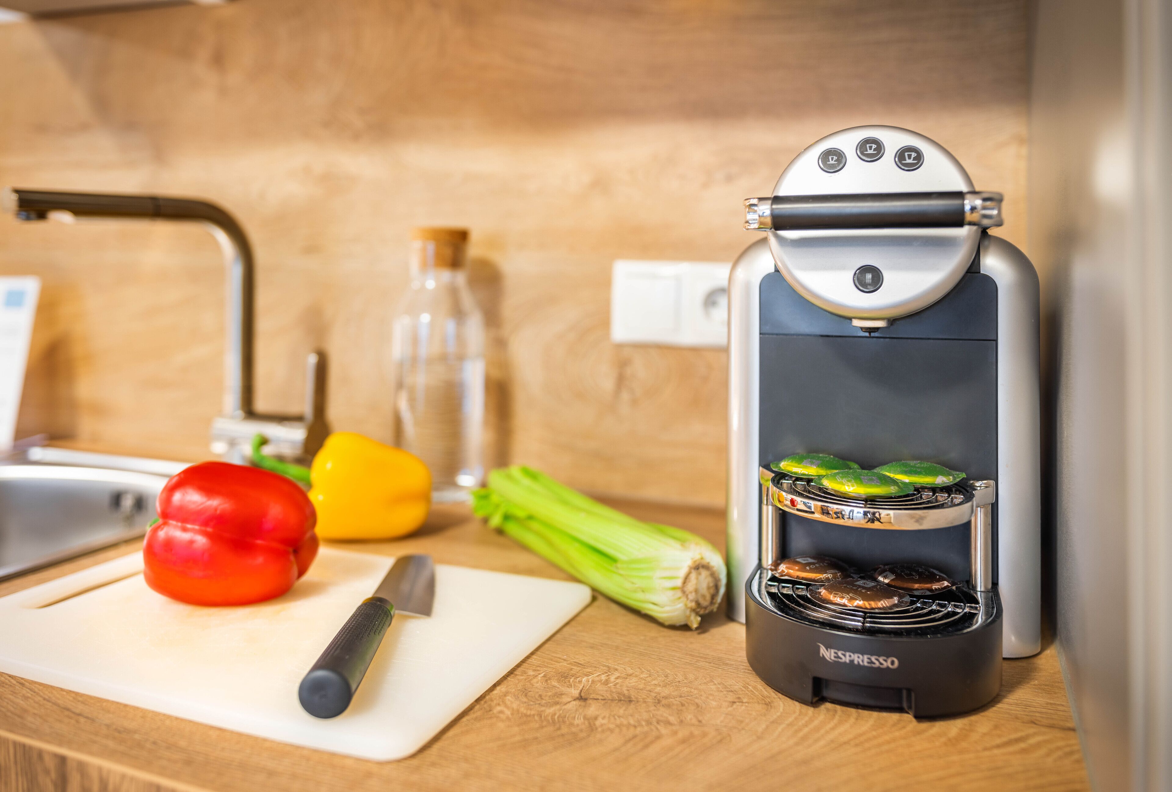 A kitchen with a Nespresso coffee machine, a cutting board with vegetables, and a knife.