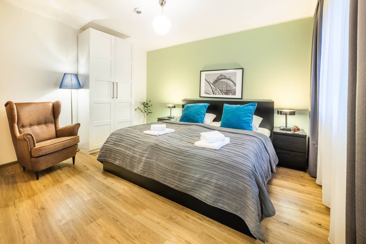 Quarto bem organizado com cama, cadeira, guarda-roupa e mesa de cabeceira.