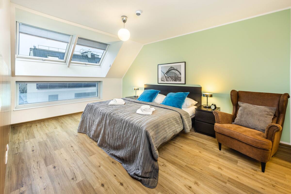 Quarto com cama, cadeira, mesa de cabeceira e janela.