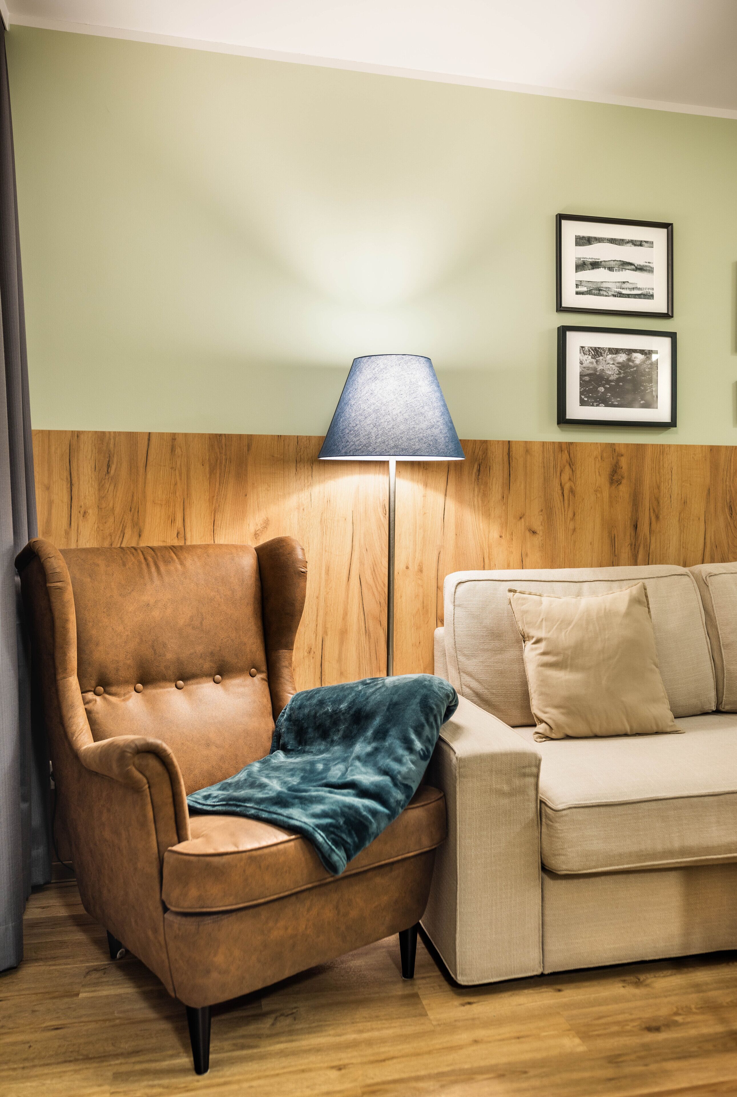 Ein Zimmer mit einem braunen Ledersessel, einer blauen Lampe und einem beigen Sofa.