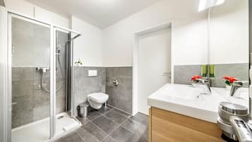 A modern bathroom with a glass-enclosed shower, a toilet, and a sink with a mirror.