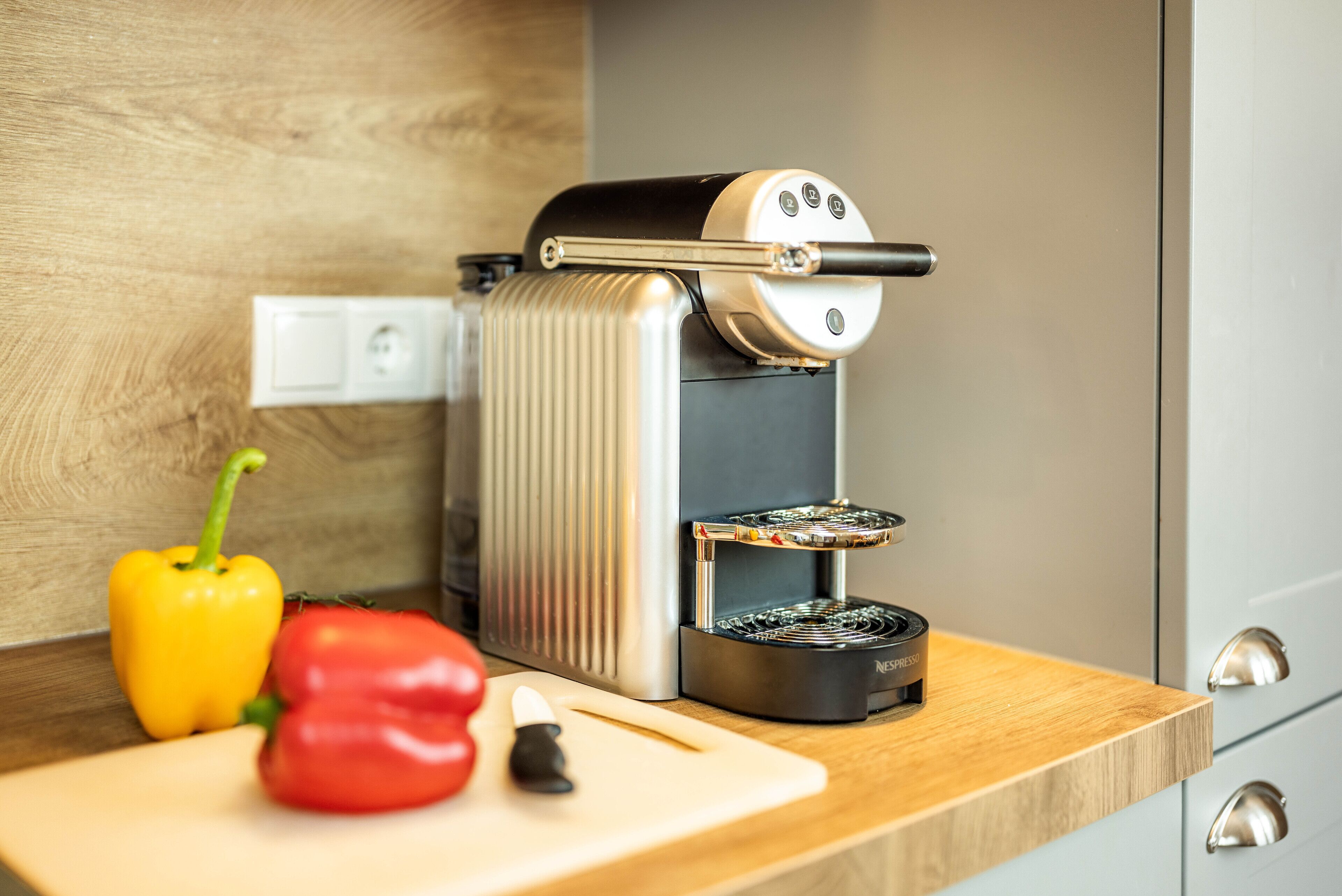 A kitchen with a coffee machine, a cutting board, and vegetables.