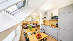 A modern kitchen with grey cabinets, a microwave, and a dining area with a wooden table and chairs. - Jimmy's Apartments Lory (Vienna)