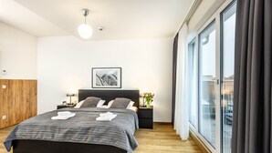A modern bedroom with a large bed, a nightstand, a framed picture, and a window with curtains. - Jimmy's Apartments Lory (Vienna)