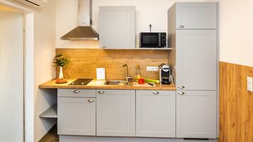 A compact kitchen with grey cabinets, a built-in microwave, and a stainless steel sink.