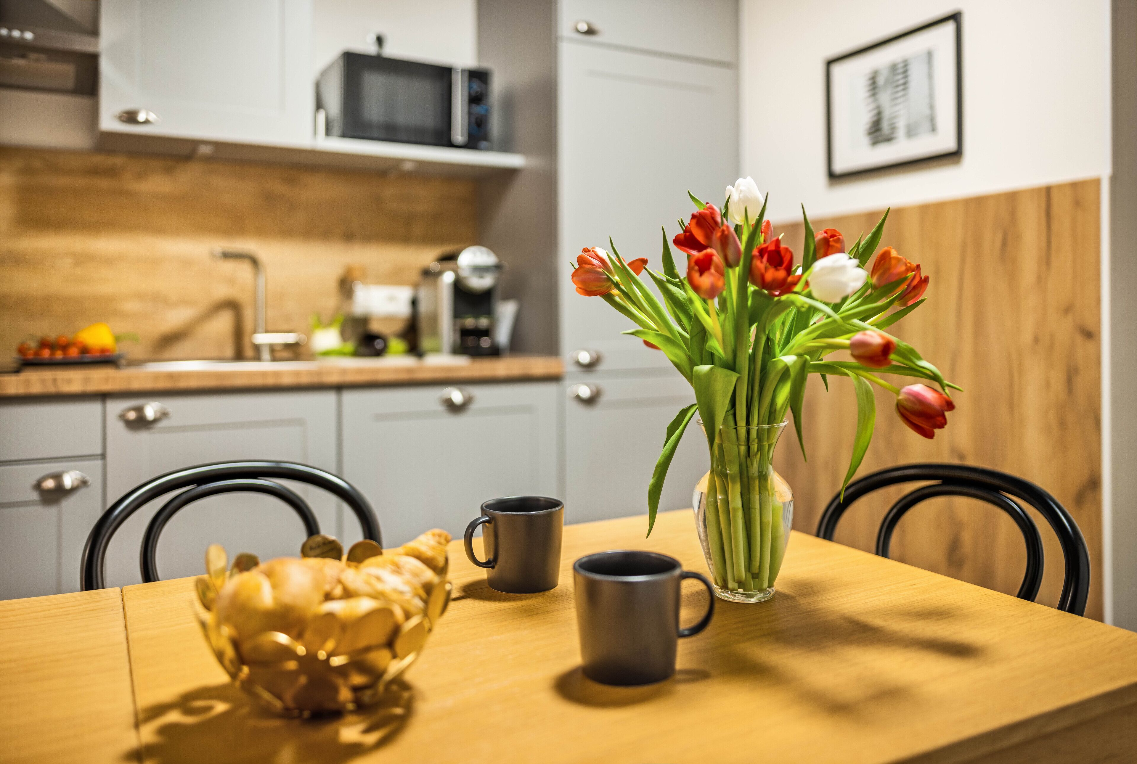 A dining table with two mugs, a vase with tulips, and a decorative shell.