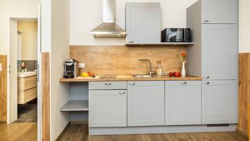 Une cuisine compacte avec des meubles gris, un plan de travail en bois, une hotte en acier inoxydable et un four à micro-ondes.