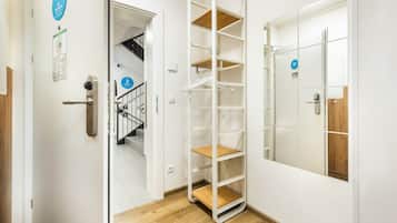 A hotel room with a wooden floor, a white door with a mirror, a metal shelf unit, and a 'No Smoking' sign.