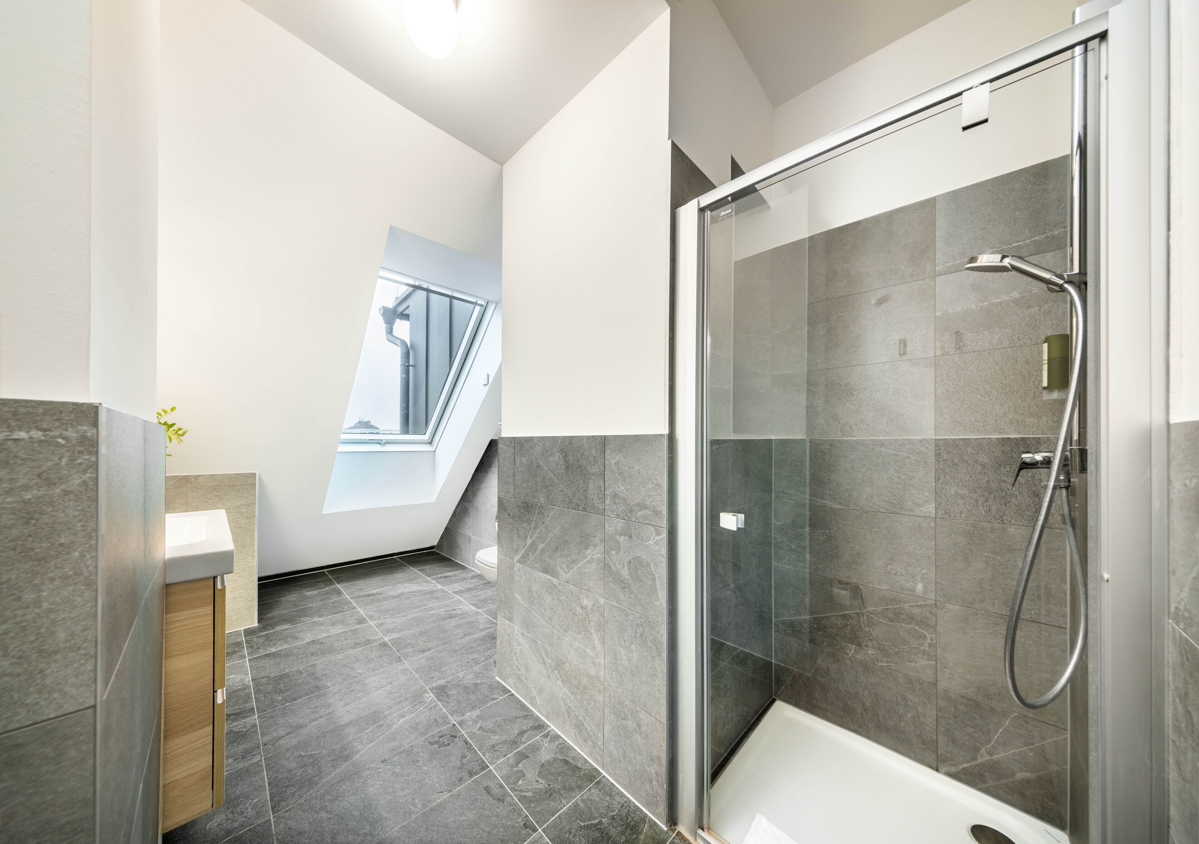 Une salle de bain moderne avec une douche à parois de verre, un meuble-lavabo en bois et une vue sur un escalier.