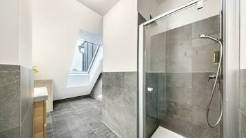 A modern bathroom with a glass-enclosed shower, a wooden vanity, and a view of a staircase.