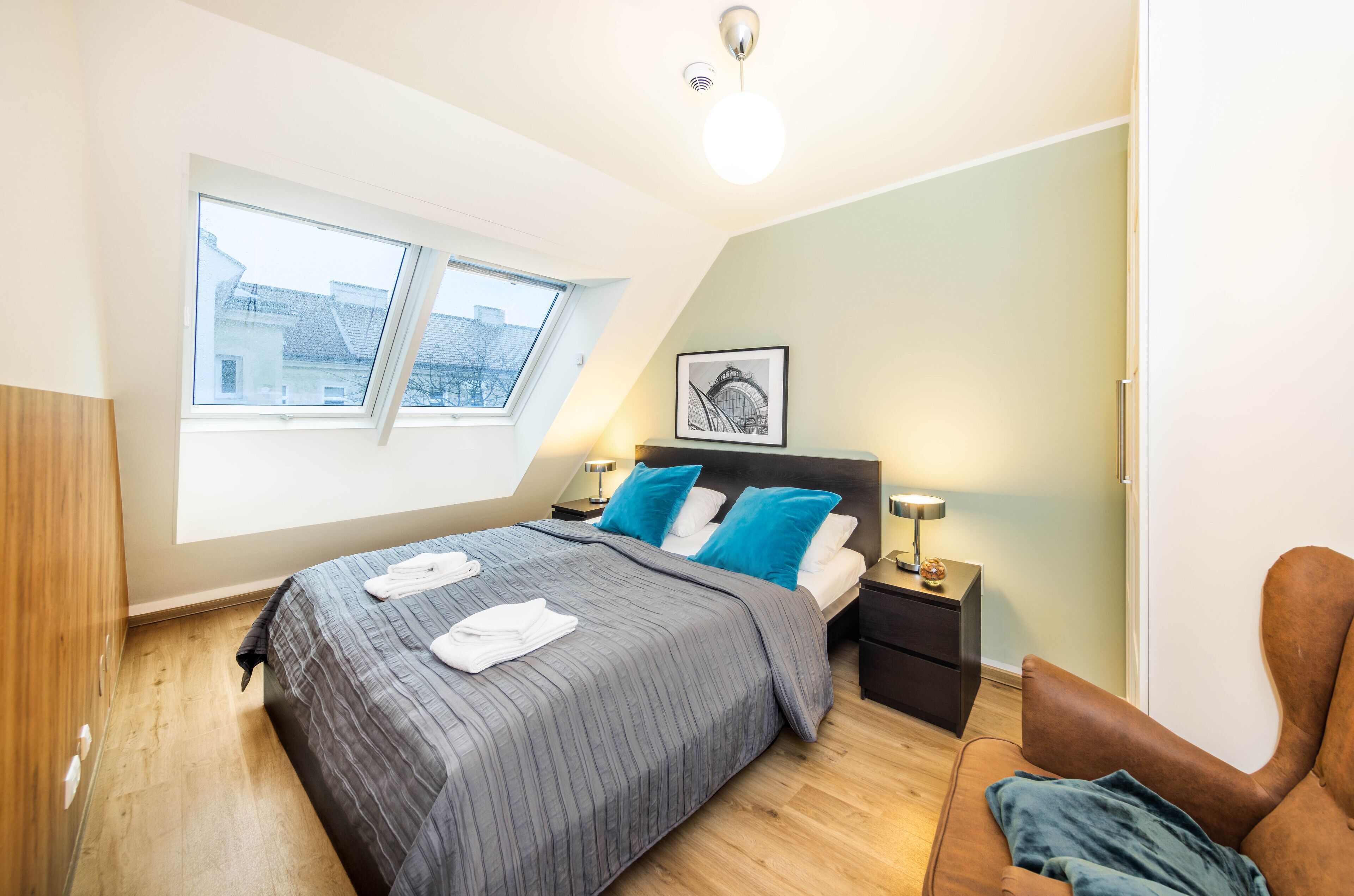 A bedroom with a bed, a nightstand, a chair, a window, and a ceiling light.