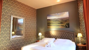 Habitación de hotel con una cama grande, dos lámparas de noche, un espejo y un cuadro de paisaje en la pared.