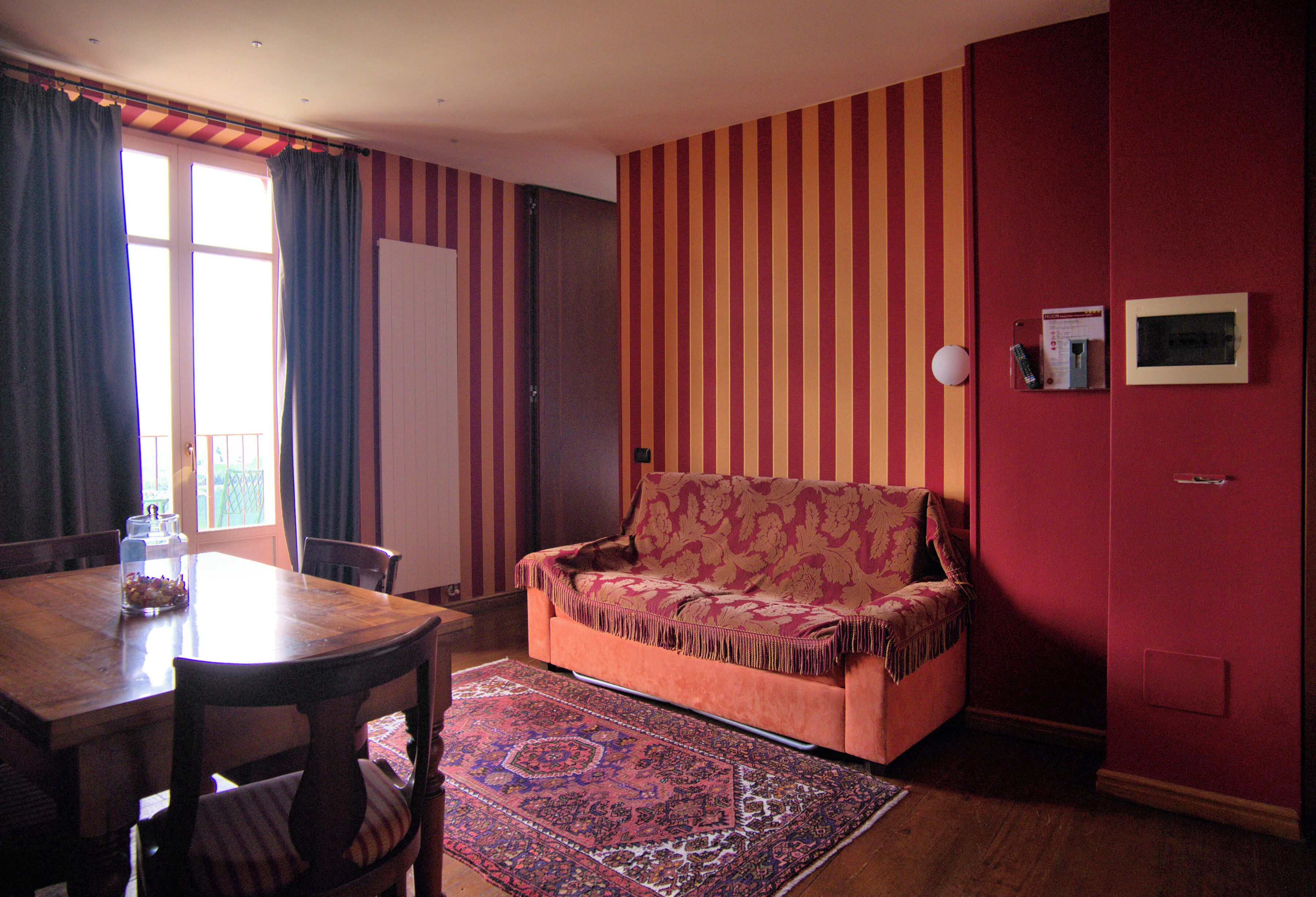 A room with a sofa, a dining table with chairs, a patterned rug, and a striped wall.