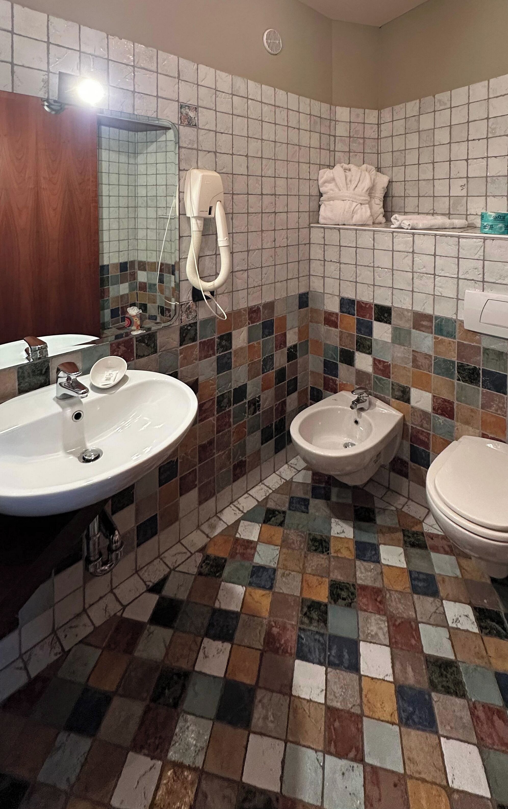 A bathroom with a tiled floor, a sink, a bidet, and a toilet.