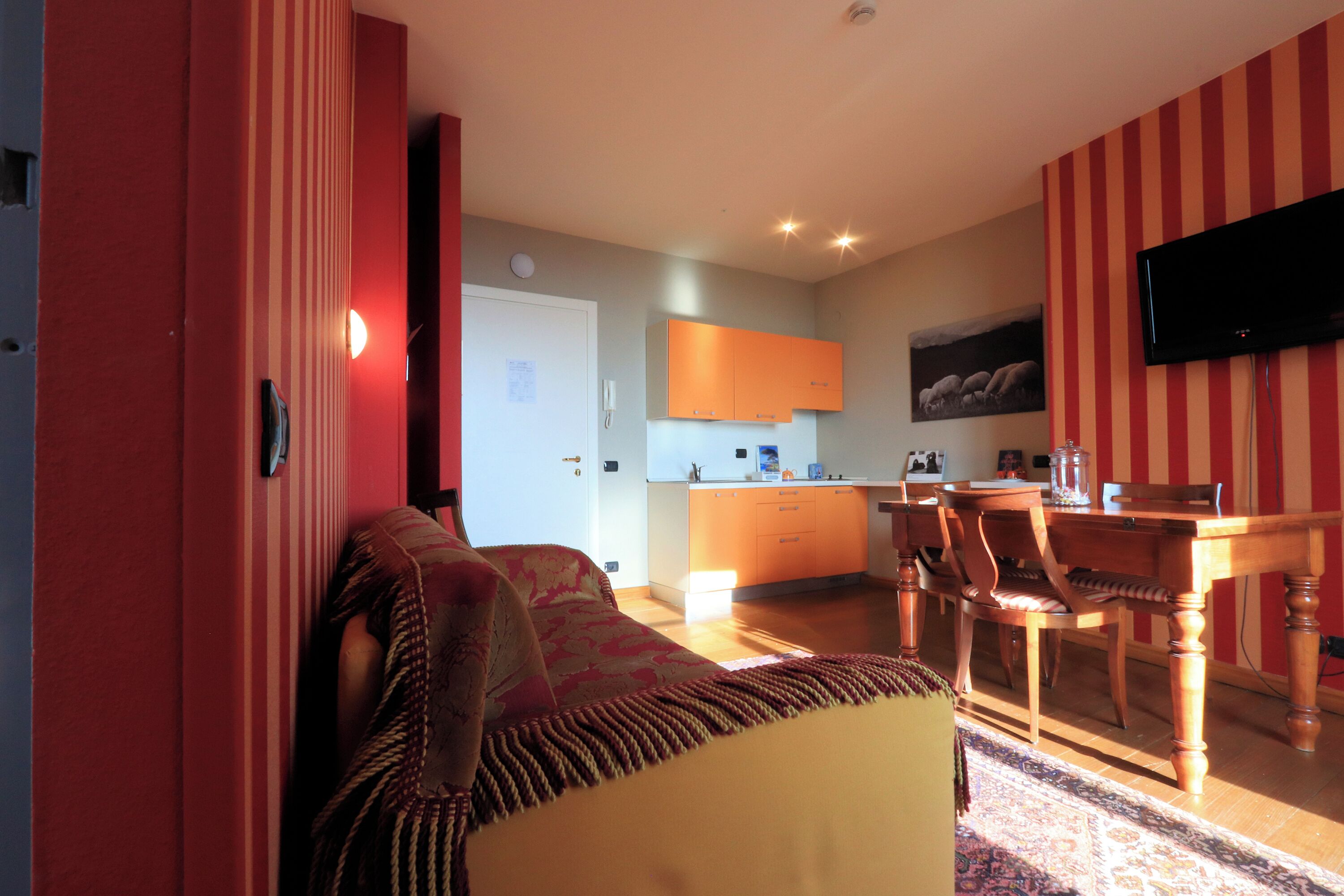 Een woonkamer met een bank, een eettafel met stoelen, een keuken met kastjes en een flatscreen televisie aan de muur.