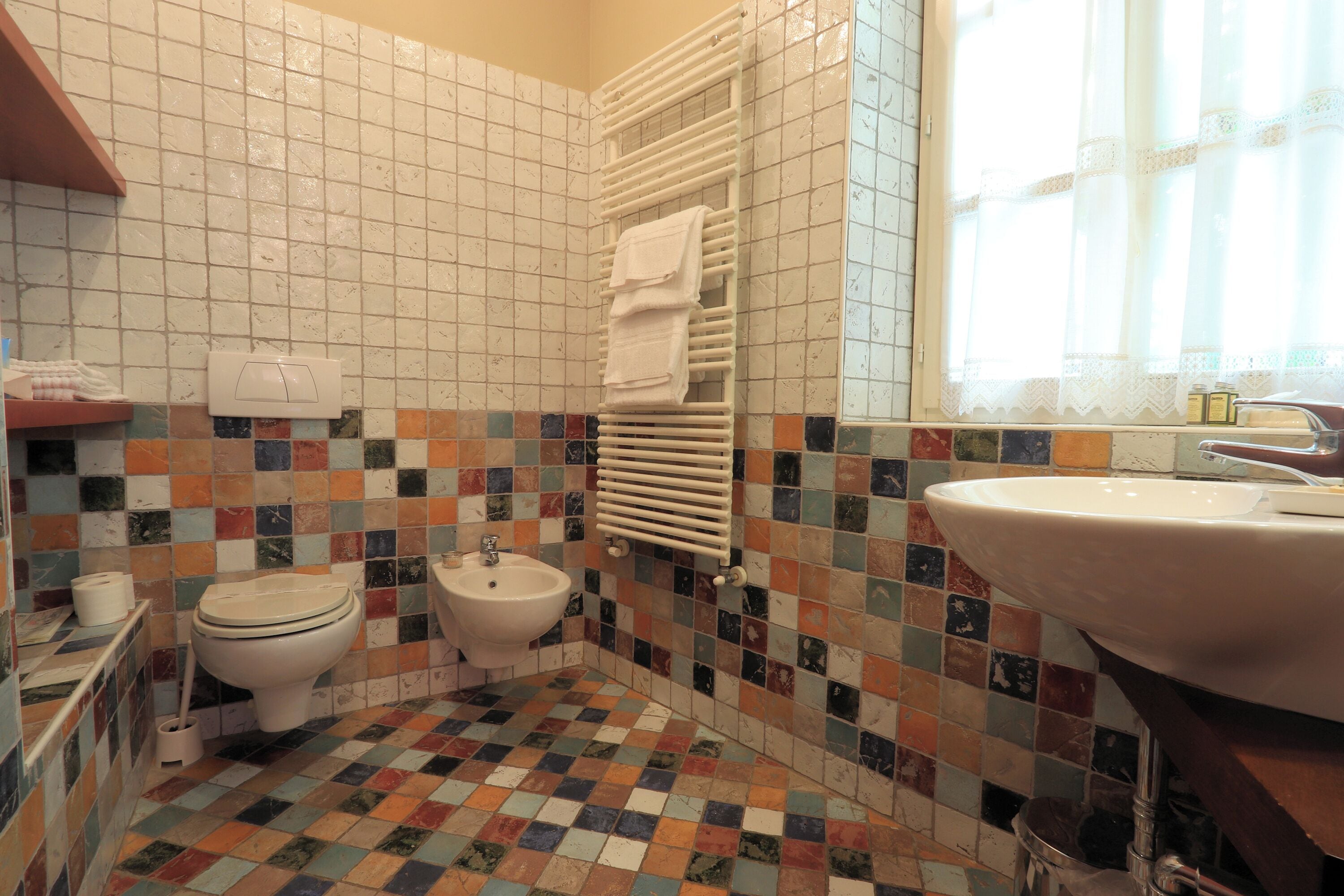 A bathroom with a tiled floor, a toilet, a bidet, a sink, and a towel rack.