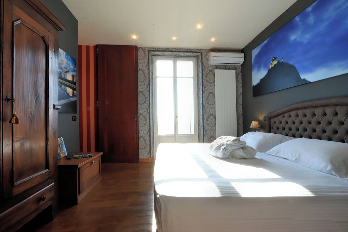 Une chambre d’hôtel avec un grand lit, une armoire, un tableau au mur et une fenêtre avec des rideaux.