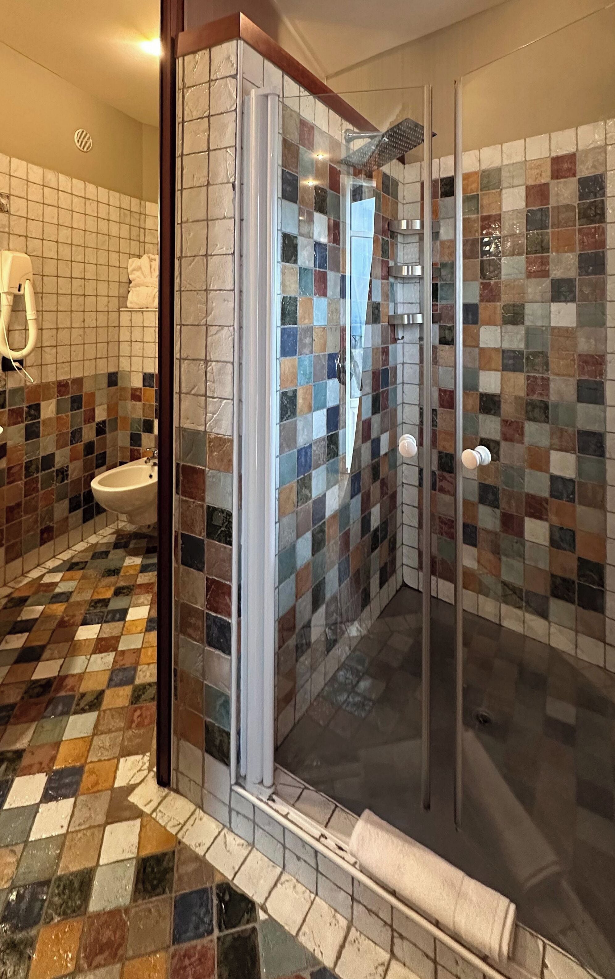 A modern bathroom with a glass shower enclosure, a bidet, and a tiled floor.